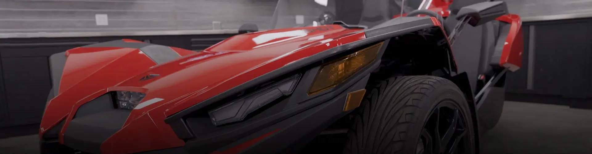 Close-up of a red Polaris Slingshot roadster featuring its angular front bodywork, headlights and front wheel.