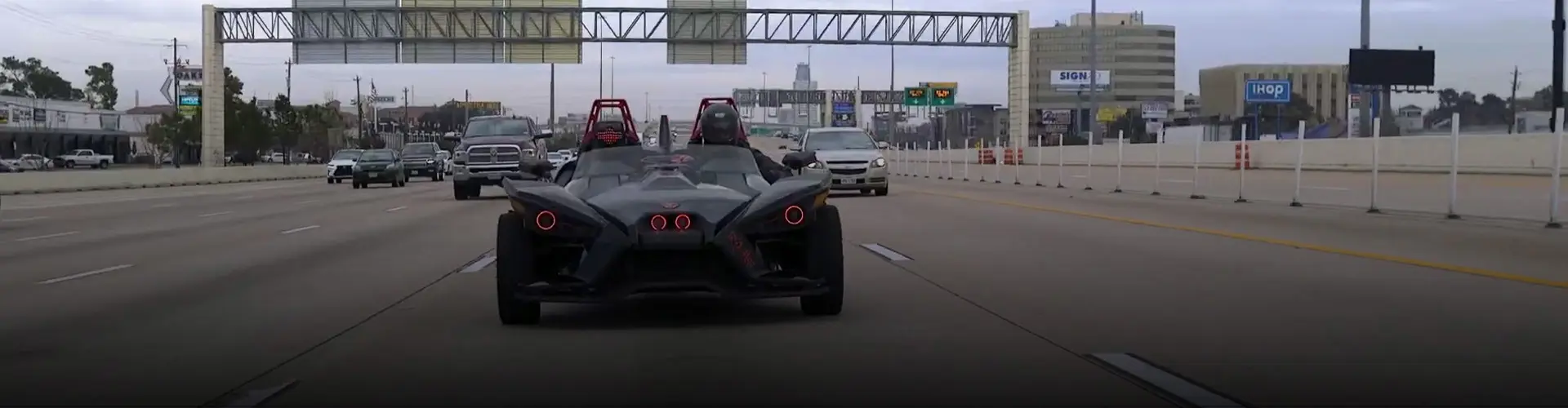 Custom black Polaris Slingshot three-wheel vehicle driving in traffic on a multi-lane Houston highway.