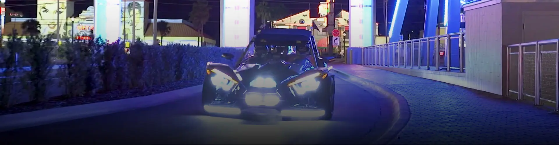 Custom Polaris Slingshot three-wheel vehicle driving through a brightly illuminated Orlando, FL district at night.