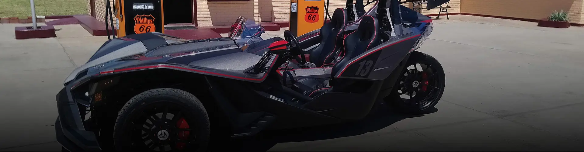 Custom gray Polaris Slingshot roadster parked beside vintage Phillips 66 gas pumps.
