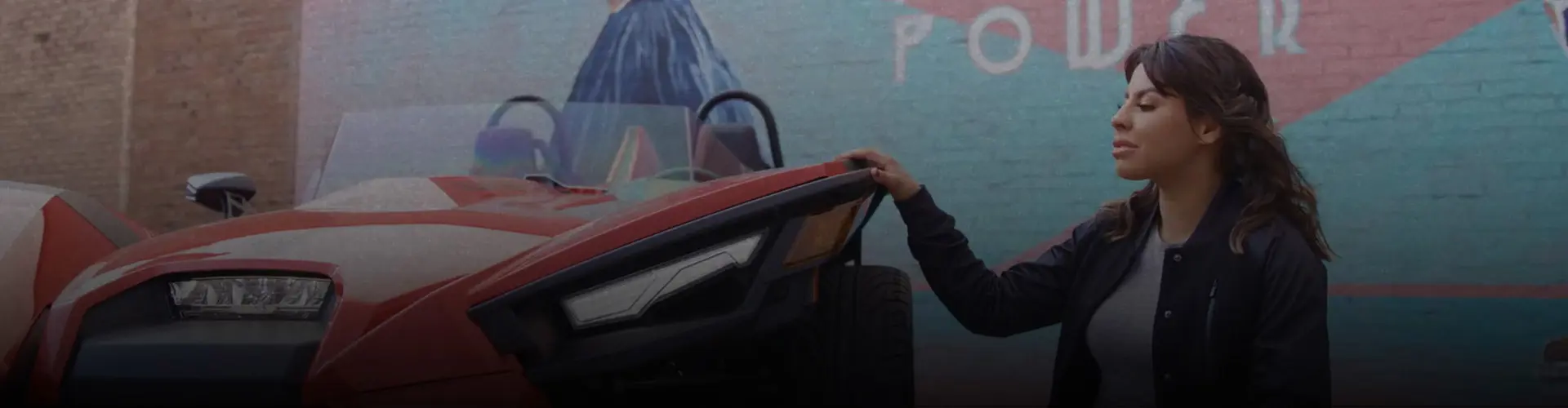 Marlen Esparza beside a red Polaris Slingshot roadster in front of a colorful Female Power mural.