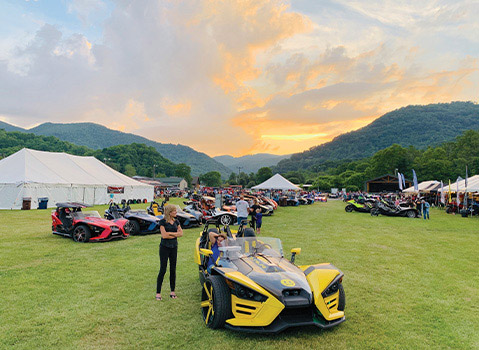 Custom Polaris Slingshot three-wheel vehicles displayed at an outdoor mountain event during sunset.