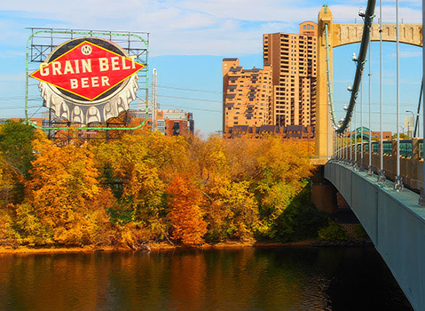 Grain Belt Beer sign beside a suspension bridge and autumn trees along the Mississippi River in Minneapolis.