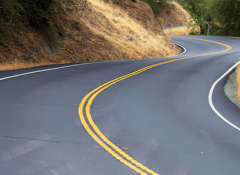 Winding paved road with sharp curves through a wooded landscape of dry grass and trees.