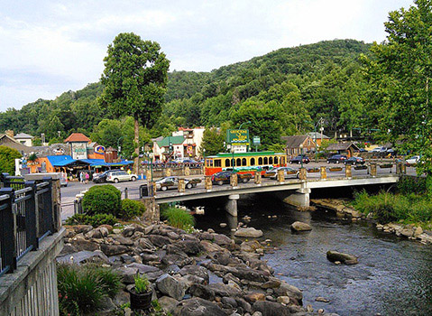 Downtown Gatlinburg with a colorful trolley crossing a bridge over a rocky stream.