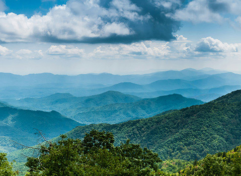 Panoramic view of forested ridges in the Great Smoky Mountains beneath a blue sky filled with clouds.