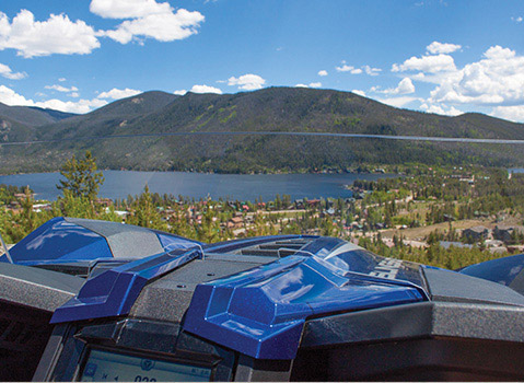 Polaris Slingshot cockpit overlooking a mountain town and blue lake through a clear windshield.