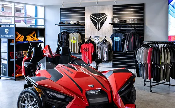 Inside view of a Slingshot dealership with a vehicle and racks full of clothing and accessories.