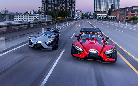 Two Polaris Slingshot vehicles being driven on the street