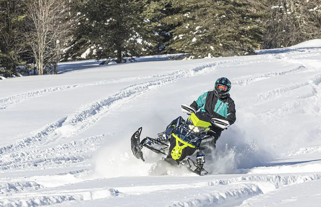 rider blasting through deep snow on a polaris switchback assault snowmobile