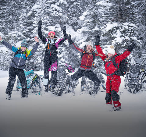 A group of people dressed with Polaris apparel in winter attire with backpacks enjoying a snowy landscape with the sun low on the horizon.
