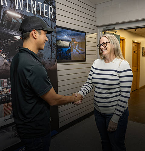 A woman shakes hands with a snowmobile technician while receiving the results of the repairs. 