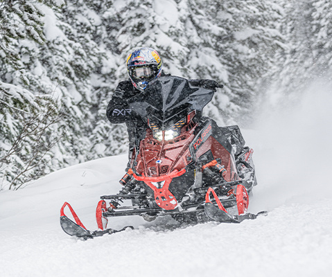 A person riding a red Polaris Snowmobile at high speed through a snowy landscape, with snow dust trailing behind.