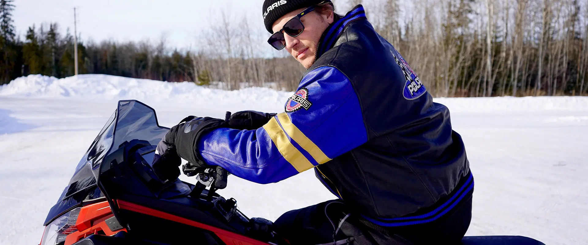 Levi LaVallee wearing Polaris jacket and beanie riding a snowmobile on a snowy trail.