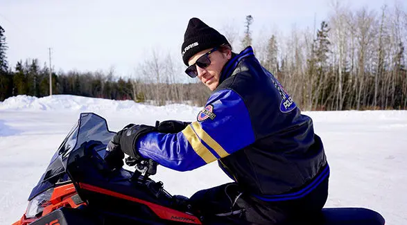 Levi LaVallee wearing Polaris jacket and beanie riding a snowmobile on a snowy trail.
