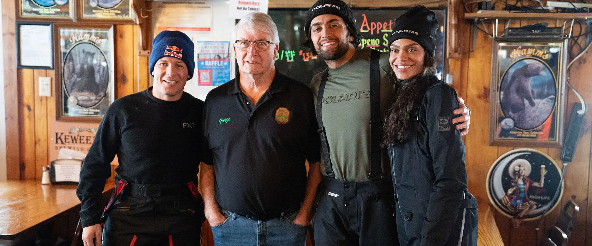 Levi LaVallee and friends, including Michelle Young and Jack Leius, wearing Polaris apparel, posing inside a restaurant decorated with vintage advertising signs.