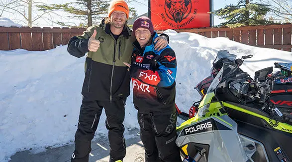 Levi LaVallee and Tyler Hubbard in West Yellowstone, Montana, wearing branded outerwear and standing next to Polaris snowmobiles.