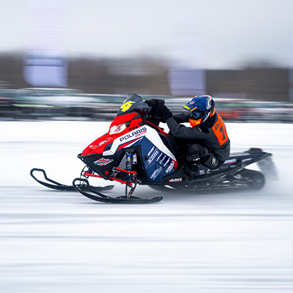 A 600 Indy Cross Country snowmobile in action on a snowy terrain, making a sharp turn near a red arrow sign indicating a left curve ahead.