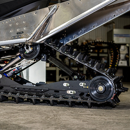 Close-up view of a 600R snowmobile’s tread and suspension system in a garage, showcasing the detailed engineering of the track with its rugged treads and complex suspension components.