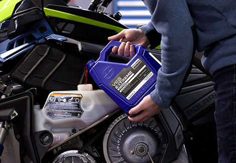 A person pouring Polaris VES Extreme engine oil into a snowmobile reservoir.