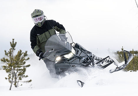 Rider on a Polaris snowmobile accelerating through deep powder snow, spraying snow behind them.