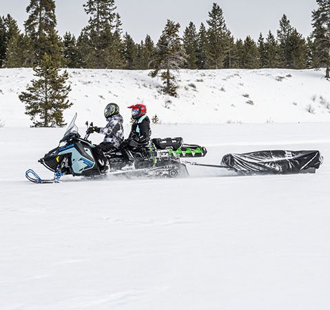 2 riders on the 2-passenger 2026 Polaris TITAN Adventure Ultimate 155 widetrack snowmobile pulling a sled.