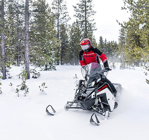 Rider cruising between trees in a forest on a 2026 Polaris TITAN SP 155 widetrack snowmobile.