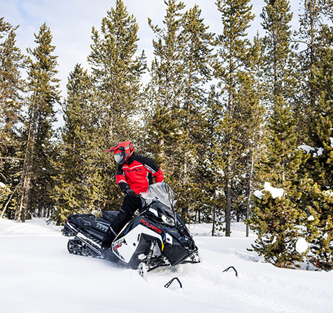 A rider on a 2026 Polaris TITAN SP 155 widetrack snowmobile looking back toward the patented BackTrak20 Rear Suspension.