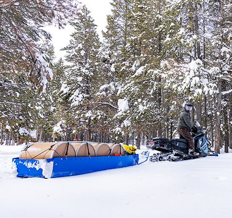 A 2026 Polaris Voyageur Adventure Ultimate 155 sport-utility snowmobile pulling a trailer-sled full of items.