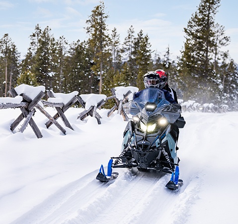 2 riders on a 2026 Polaris Voyageur Adventure Ultimate 155 sport-utility snowmobile showcasing the high-clearance A-arms and TrailBreaker skis.