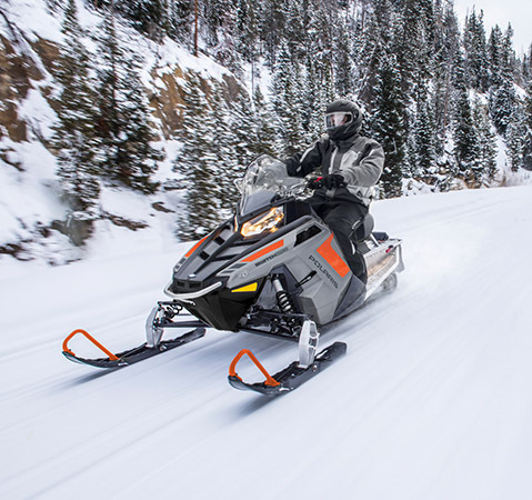 Front-end view of a Rider cruising on a trail with a Polaris snowmobile featuring the 550 Liberty engine.