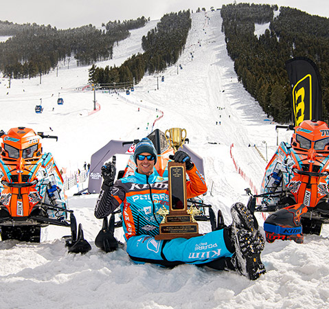 A Polaris racer posing with a trophy and the Polaris snowmobiles featuring the Patriot 9R engine that won it.