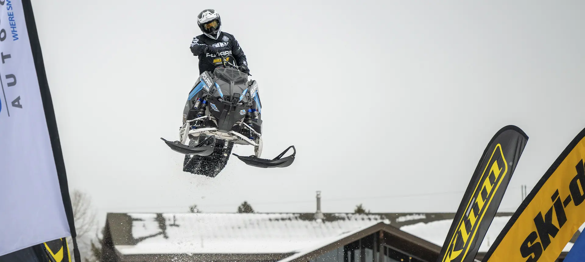 Andy Thomas jumping a black and blue Polaris snowmobile over a snowy event course.