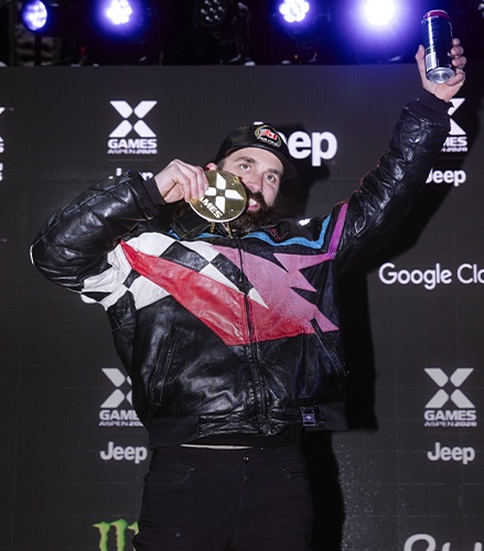 Brett Turcotte holding a gold X Games medal and raising an arm at the awards ceremony.