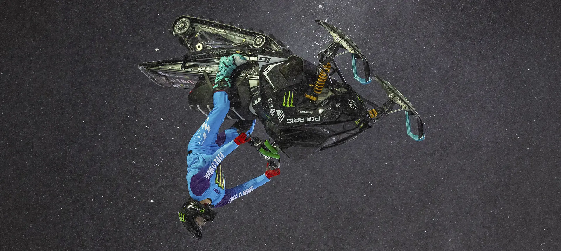 Overhead view of Brett Turcotte performing an aerial stunt on a black Polaris snowmobile.