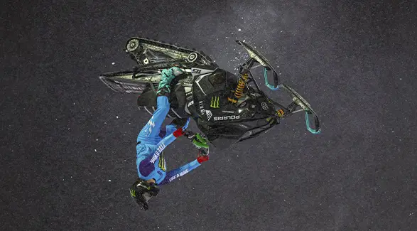 Overhead view of Brett Turcotte performing an aerial stunt on a black Polaris snowmobile.