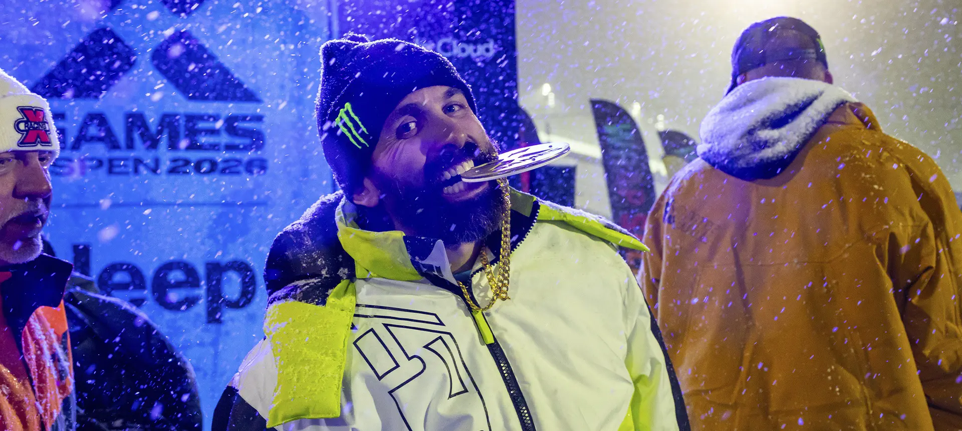 Brett Turcotte holding a medal between their teeth during a snowy X Games awards ceremony.