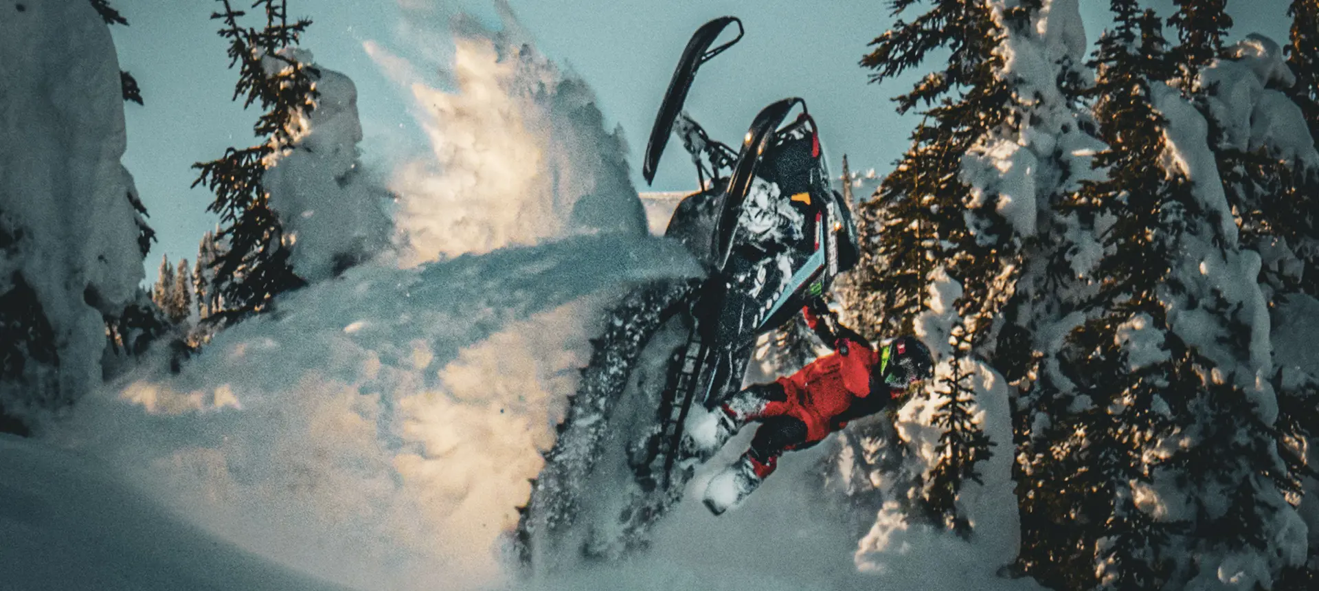Brett Turcotte carving a black Polaris snowmobile through deep powder in a snow-covered forest.