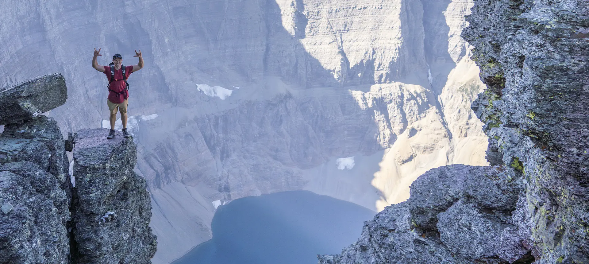 Caleb Kesterke standing on a rocky ledge above a deep alpine lake surrounded by towering mountain cliffs.