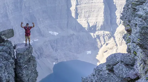 Caleb Kesterke standing on a rocky ledge above a deep alpine lake surrounded by towering mountain cliffs.