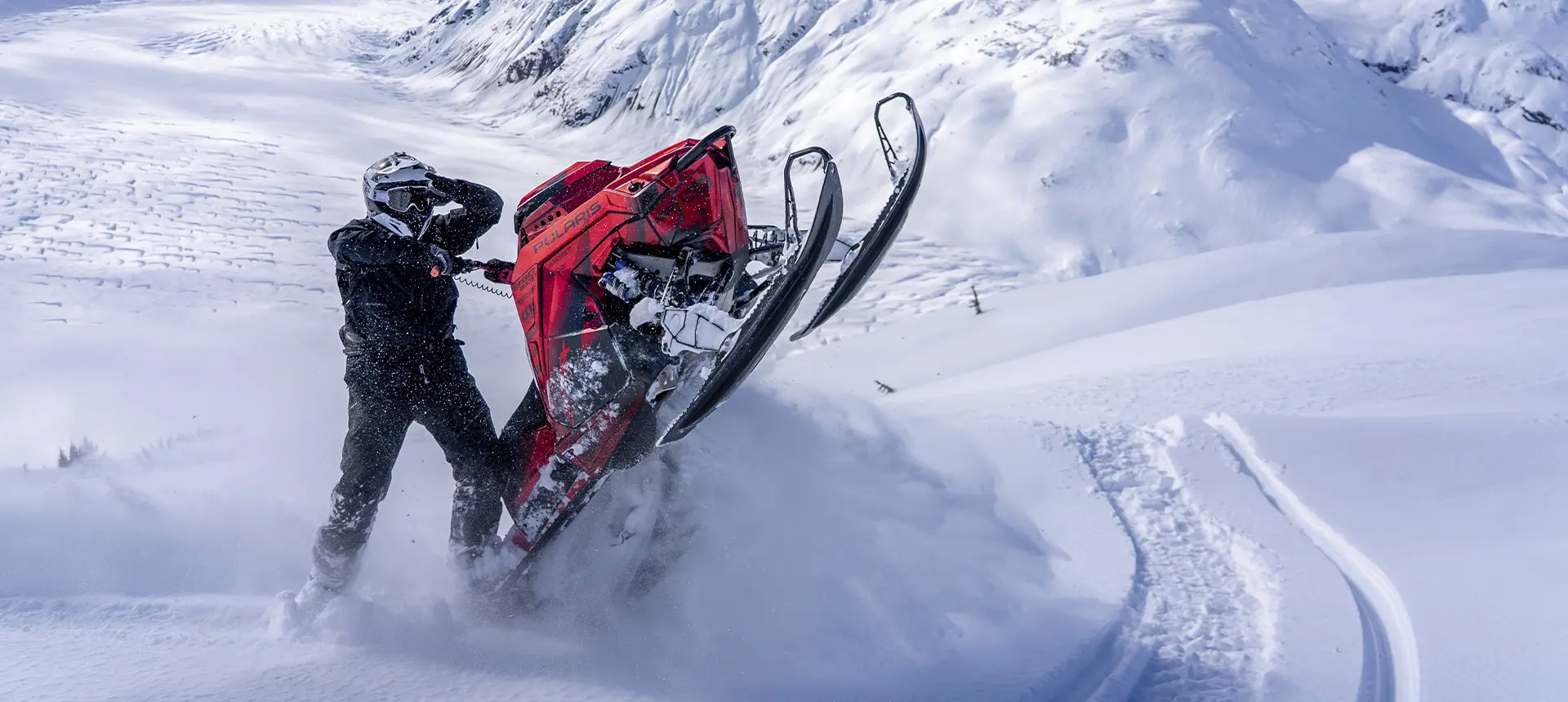 Caleb Kesterke maneuvering a red Polaris RMK snowmobile through deep powder on a snowy mountain slope.