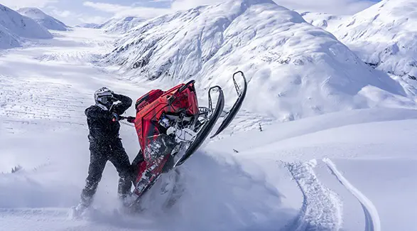 Caleb Kesterke maneuvering a red Polaris RMK snowmobile through deep powder on a snowy mountain slope.