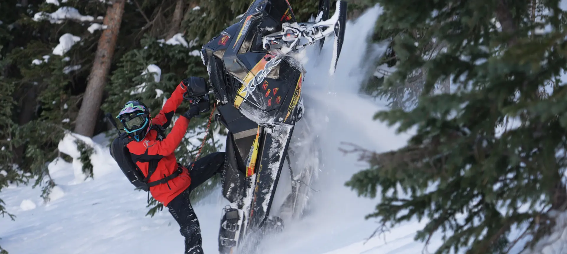Chris Burandt maneuvering a black Polaris snowmobile through deep powder in a snow-covered evergreen forest.