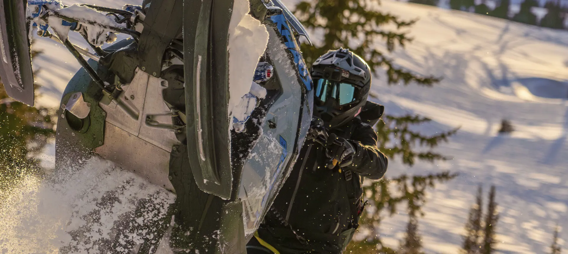 Kyle Pulsifer maneuvering a blue Polaris snowmobile through deep powder on a sunlit mountain slope.