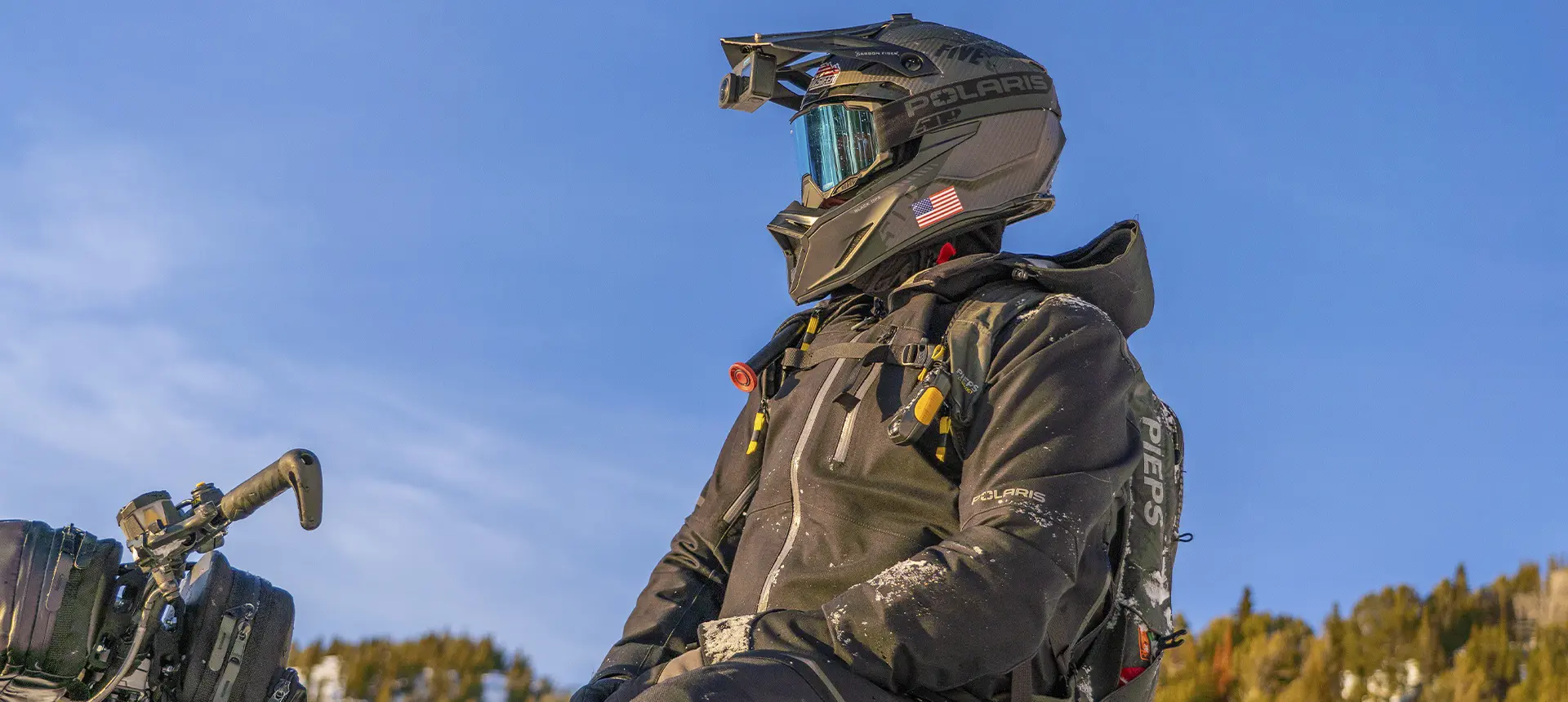 Kyle Pulsifer wearing a helmet camera, goggles and avalanche safety gear beneath a clear blue sky.