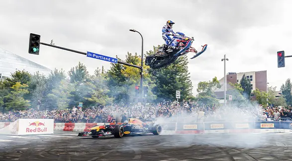 Levi LaValle jumping over a Red Bull Formula 1 car during a crowded city motorsports event.