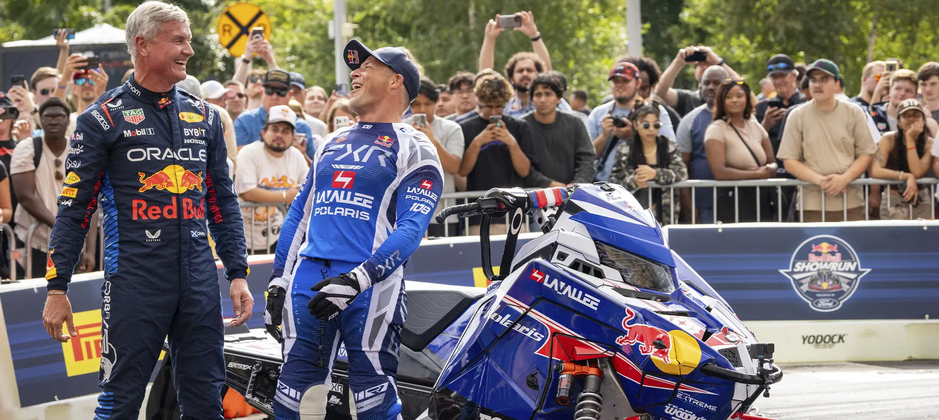 Levi LaValle and another motorsports athlete beside a custom Polaris snowmobile as spectators watch at an outdoor Red Bull event.