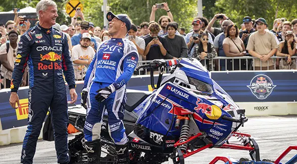 Levi LaValle and another motorsports athlete beside a custom Polaris snowmobile as spectators watch at an outdoor Red Bull event.