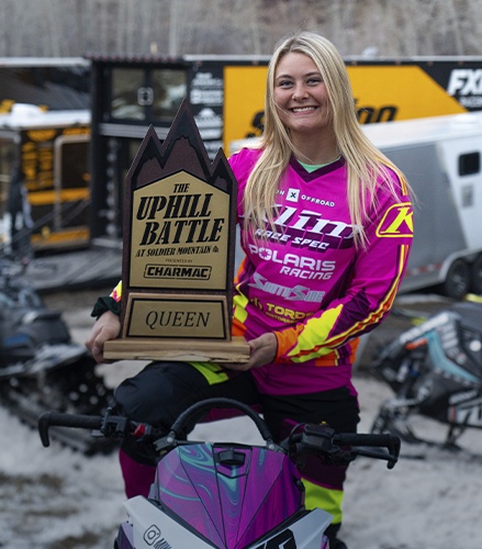 Polaris Racing competitor Mikaela Grönlund holding The Uphill Battle Queen trophy at a snowmobile racing event.