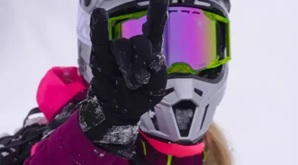 Close-up of Mikaela Grönlund in colorful winter gear and mirrored goggles making a hand gesture.